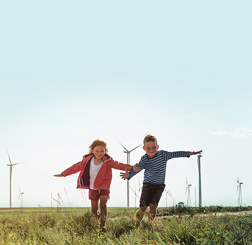 A boy and a girl running in a grass field with windmills in the background